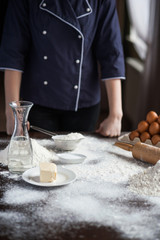 Image of hard working male cook or baker with dark skin wears apron, sheets well made dough, going to bake tart, isolated over black chalk background. Unrecognizable African American chef on kitchen