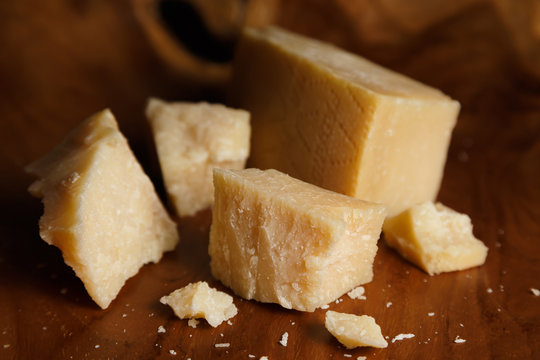 Pieces of parmesan or parmigiano reggiano cheese on a wooden board. Parmesan cheese uses in pasta, risotto and salads. Close-up.