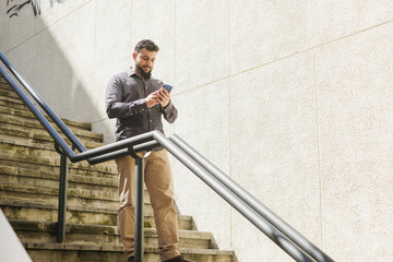bearded man looking amartphone while walking down the stairs