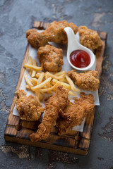 Wooden serving board with roasted breaded chicken, french fries and sauce, selective focus, vertical shot