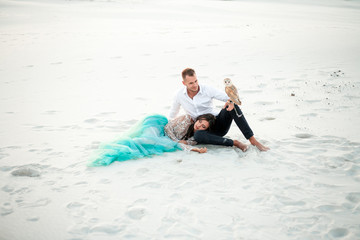 Bride and groom with small owl are sitting in desert on background of white sand.