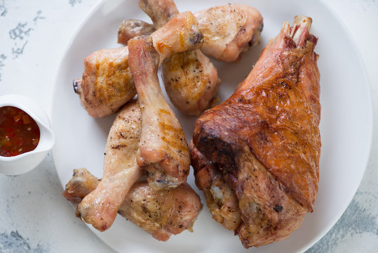 Above view of barbecued turkey and chicken legs with sauce on a white plate, horizontal shot, closeup