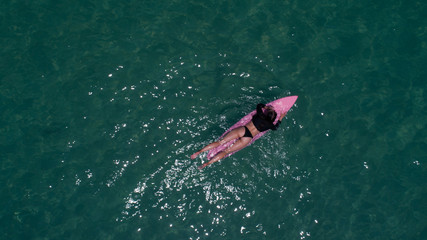 Aerial top view of beautiful young woman in swimsuit with pink surfboard enjoying her holiday in amazing clear sea water