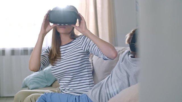 Medium shot of curious little boy and his young mother wearing VR headsets and looking around in amazement