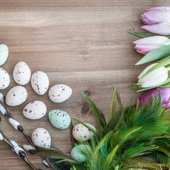 Easter chocolate eggs, feathers and pastel colored tulips on rustic wooden background  