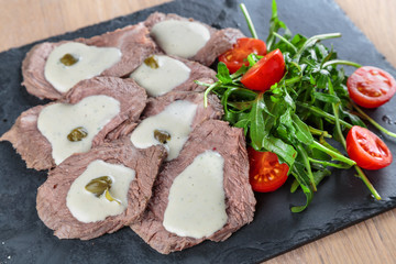 boiled beef tongue with sauce, capers and greens on a black granite tile
