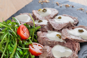 boiled beef tongue with sauce, capers and greens on a black granite tile