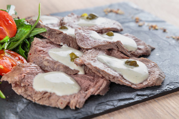 boiled beef tongue with sauce, capers and greens on a black granite tile