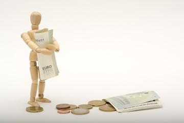 A wooden person stands and holds money, on the ground lying coins and euro banknotes (money)...