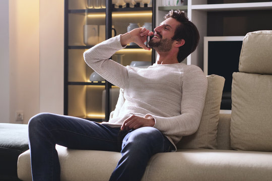 A Man In Her Living Room Relaxes On Her Chaise Longue Or Sofa, Looks Out The Window, Uses The Phone And Enjoys Comfort And Rest. Concept Of: Home, Relaxation And Comfort.