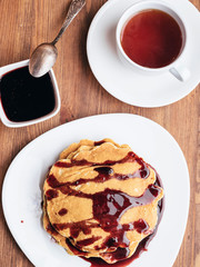 pancakes with cherry jam on a white table. a cup of tea. breakfast