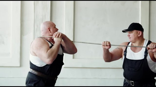 Two very powerful men are doing incredible thing with metal bar. Man bends metal bar while his friend holds it.