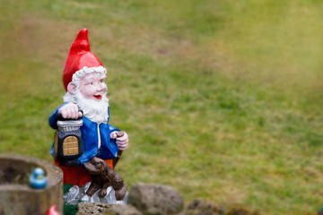 Happy garden gnome dwarf with a lantern on a weathered green lawn with copy space