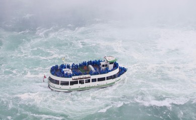 Boat with tourists enjoying the beautiful and impressive panorama of the Niagara Falls in Ontario (Canada) on a bright autumn day with water crashing down the falls onto rocks creating a lot of mist