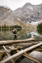 Adventure Backpacker wearing a Blue Hat Walking on a Log by a Mountain Lake