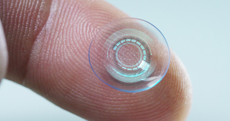Macro shot of a finger holding a contact lens technology with a chip to see better in both eyes and...