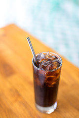 Glass of cola and ice with a reusable metal drinking straw on a wood table