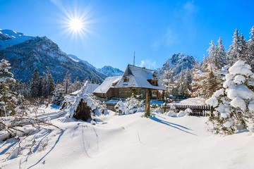 Small wooden house in winter landscape near Morskie Oko lake with sun on blue sky, Tatra Mountains, Poland