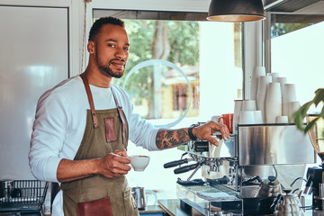 An African-American barista making a coffee with the professional coffee machine, at the coffee shop.
