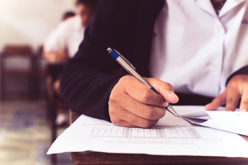 Close up to students writing and reading exam answer sheets exercises in classroom of school with stress.