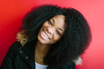 Young beautiful African American girl in a black coat smiling on red background