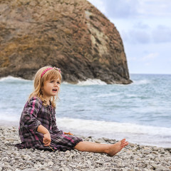 Happy little girl sitting along the ocean beach