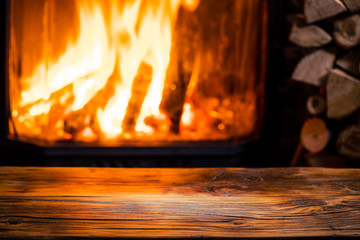 Old wooden table and fireplace with warm fire at the background.