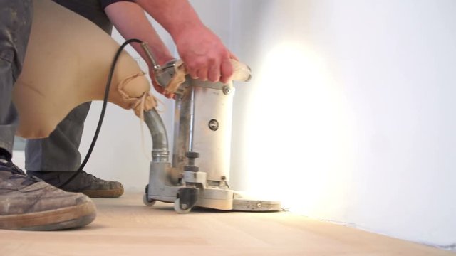 Grinding floor surface with grinding machine. Repair in the apartment. Carpenter grinder parquet in a narrow corner with a small machine