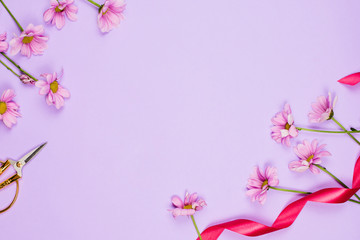 Fototapeta na wymiar Flatlay frame arrangement with violet daises, scissors and ribbon, violet background, copyspace