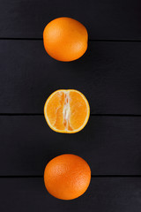 Whole and chopped oranges on a black background, citrus in retro style, copy space, a lot of oranges on a wooden background, a circle of tropical fruits on the table, fruits in the style of minimalism