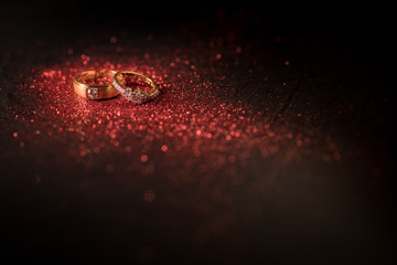 Gold wedding rings with red glitter and red bokeh on black background.