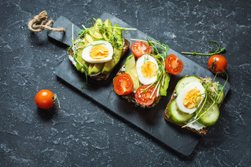 Tasty sandwiches with egg, avocado and vegetables on stone black background