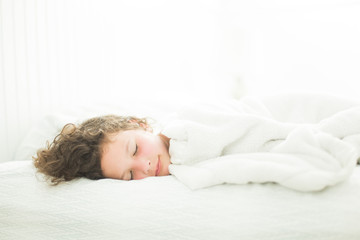 Fototapeta na wymiar Child asleep in white light-filled bedroom