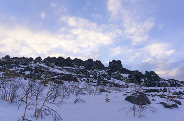 blue morning sky above a rocky ridge in the winter mountains with stone placers and a crooked birch...
