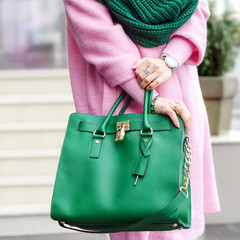 Bag in female hands. Bright leather bag. accessories. Pink coat and green bag. 