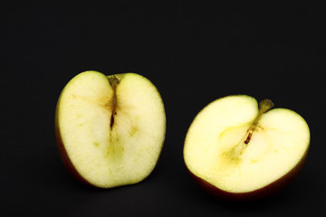 One red ripe apple sliced in half showing apple pips isolated on a black background