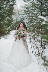Fototapeta na wymiar Portrait of a bride in a chic white dress among snow-covered fir branches