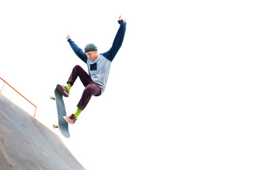 The teenager skateboarder in the cap does a trick with a jump on the ramp in the skatepark....