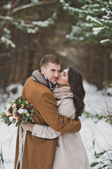 The newlyweds hug each other against the background of the winter fore