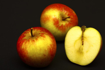 Two whole red apples and one sliced in half isolated on a black background