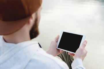 Hipster person holding in hands digital tablet with empty blank screen, man photograph on computer on background nature outdoor landscape mock up technology blur male hands tourist using gadget
