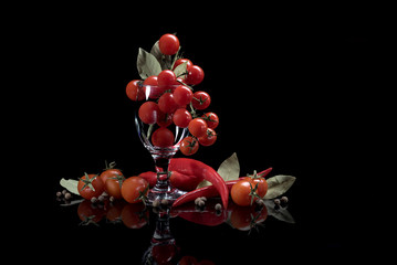 Fototapeta na wymiar Red tomatoes in a glass, spicy red pepper, bay leaf, pepper peas on a black background.