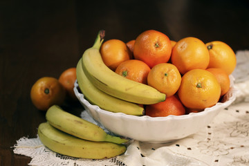 A nice basket of fruit (bananas and oranges) on a wooden table with a white cloth