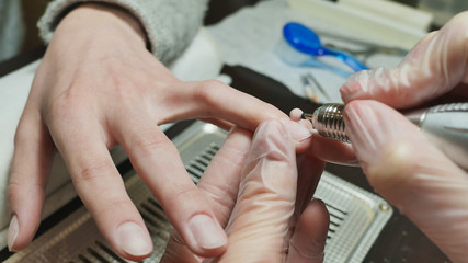 Grinding of a cuticle and side rollers. Woman's hands at manicure procedures.