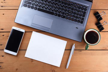 Laptop and cup of coffee on a wooden background, workstation on an old desk, smartphone and a notebook, pen and glasses in the workplace, designer workstation, office