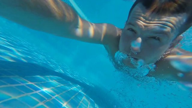 SLOW MOTION: Man diving in hotel swimming pool, sea or ocean underwater view. Swimmer jumping in to the water. Sun underwater over blue sunny sky background. Shot FullHD 120fps video.