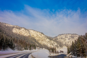 Outdoor view of winter road covered with heavy snow and ice in the forest and small river at one...