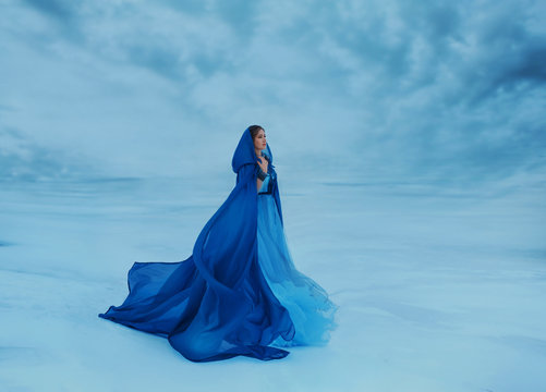 A wanderer in a blue cloak that waving in the wind. The Queen in a luxurious blue dress amidst a frozen valley covered with ice, snow and clouds, a fabulous place where heaven meets the earth. Art