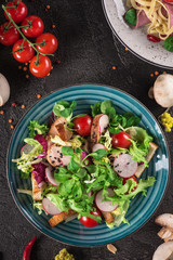 Fresh vegetable salad with grilled chicken breast - tomatoes, radish and mix lettuce leaves. Chicken salad. Healthy food. Black background. Top view