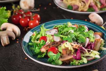 Fresh vegetable salad with grilled chicken breast - tomatoes, radish and mix lettuce leaves. Chicken salad. Healthy food. Black background. Top view